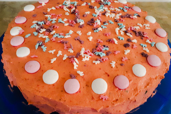 Torte auf blauer Tortenplatte mit rosa Erdbeercreme verziert mit Rosa und weißen Minzschokoladenlinsen und Bunten Einhornzuckerstreuseln