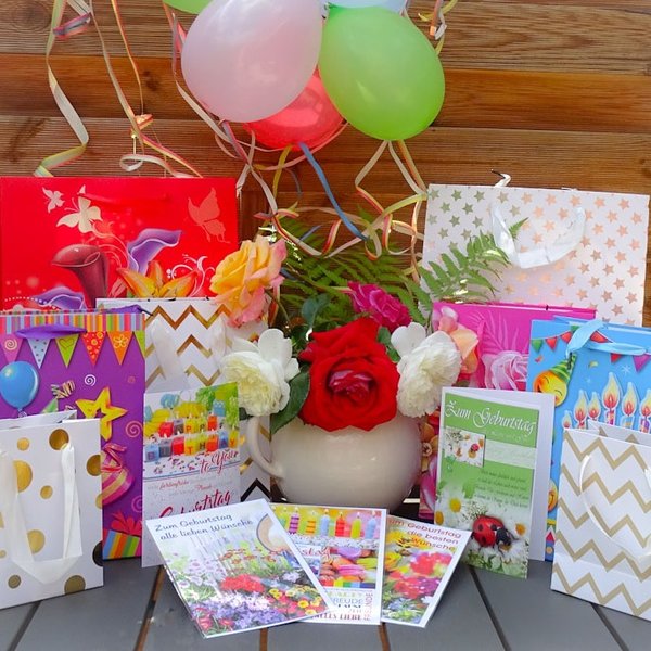 Geschenktüten und Geburtstagskarten auf einem Tisch mit Blumen, Luftballons und Papierschlangen