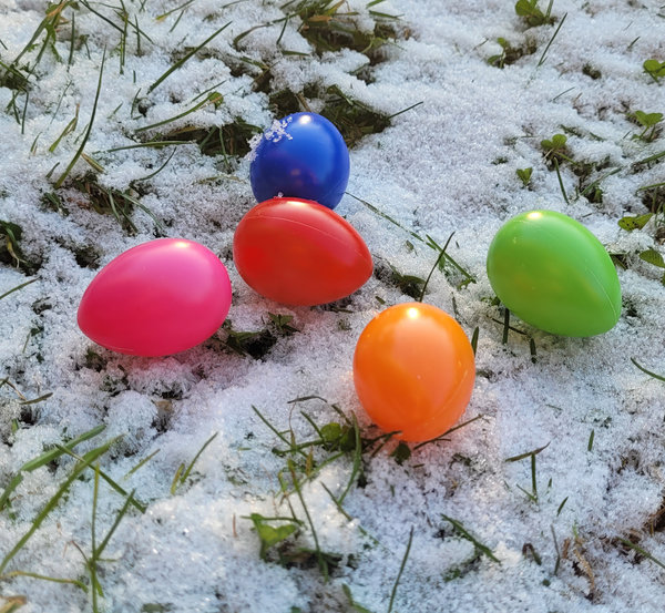 Bunte Plastikostereier auf verschneiter Wiese. Farbenfrohe Ostereier läuten den Frühling ein